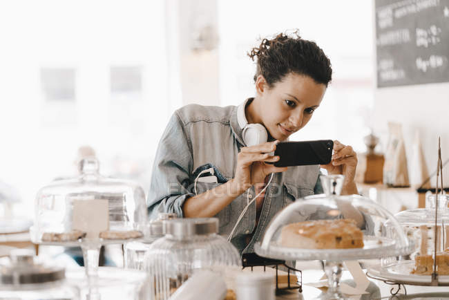 Frau fotografiert Kuchen im Café mit ihrem Smartphone — Stockfoto