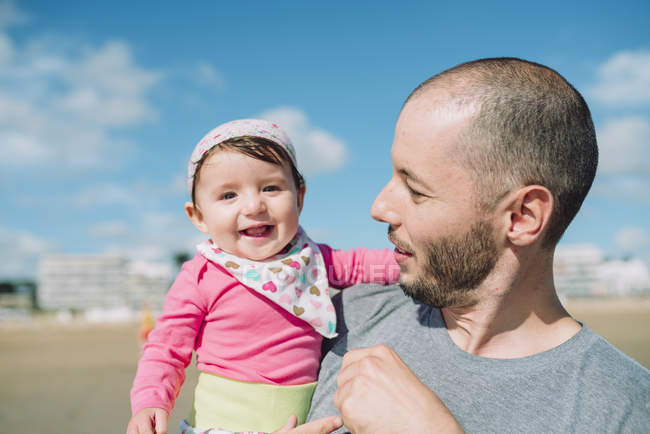 France, La Baule, portrait of smiling baby girl on father's arms on the beach — Stock Photo