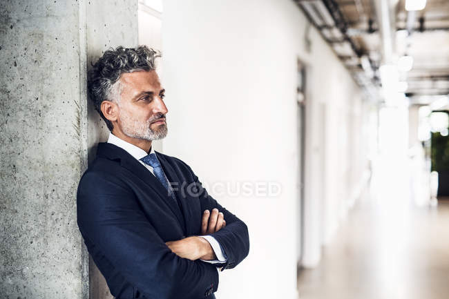 Homme d'affaires mature appuyé sur le mur dans le bureau et la pensée — Photo de stock