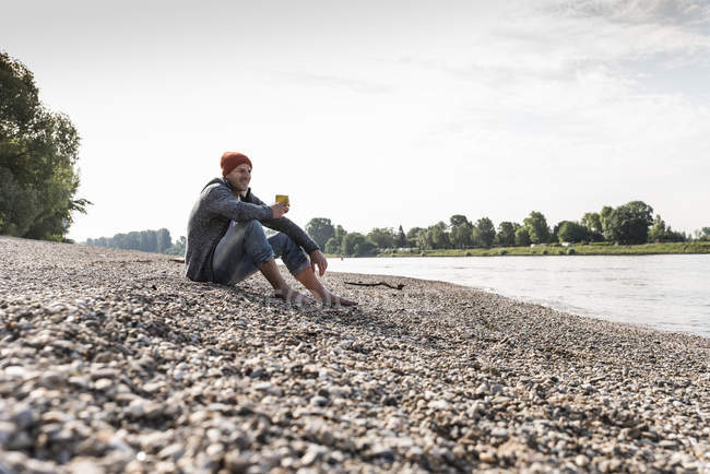 Homme mûr portant un bonnet rouge et buvant du café au bord du Rhin — Photo de stock