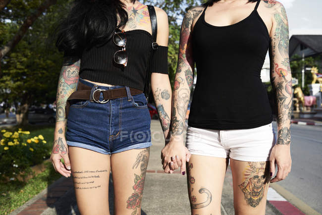 Tätowiertes lesbisches Paar, das im Sommer auf der Straße Händchen hält — Stockfoto