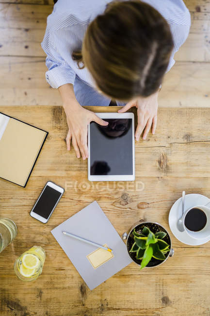 Top view of woman at wooden desk with notebook, cell phone and tablet — Stock Photo