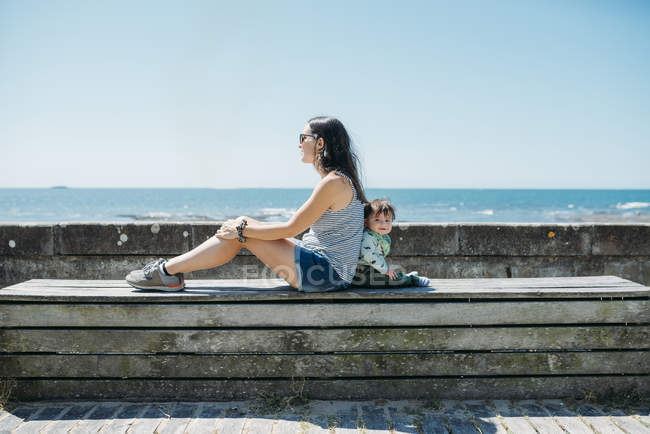 Frankreich, Mutter und Baby Rücken an Rücken auf einer Bank an der Strandpromenade — Stockfoto