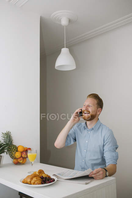 Laughing businessman on the phone at breakfast table at home — Stock Photo