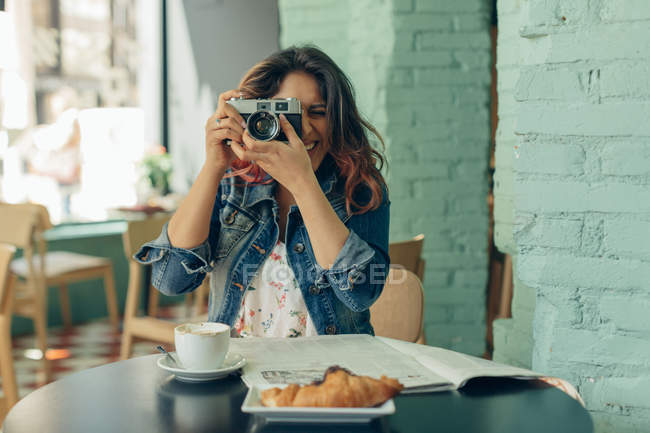 Rindo mulher sentada no café tirando fotos com câmera — Fotografia de Stock