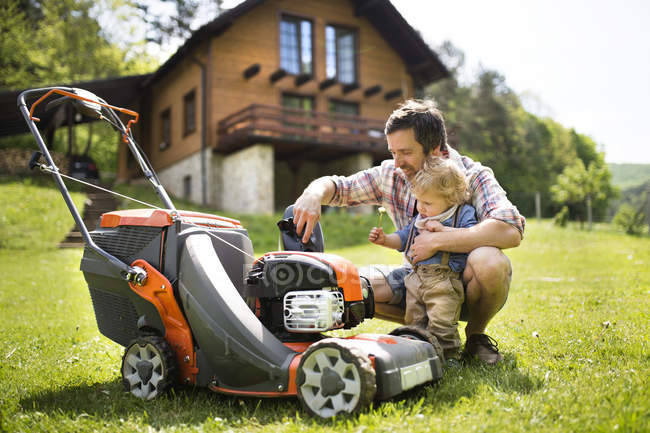 Pai com seu filho pequeno e cortador de grama — Fotografia de Stock