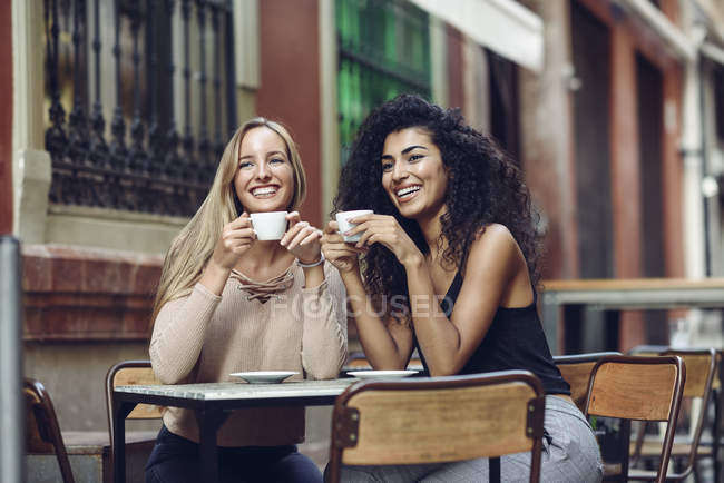 Two happy friends drinking coffee in sidewalk cafe — Stock Photo