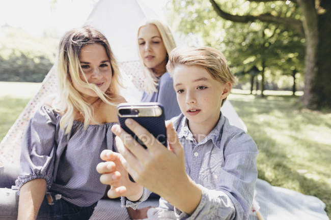 Due giovani donne e un ragazzo che si fanno un selfie accanto a teepee in un parco — Foto stock