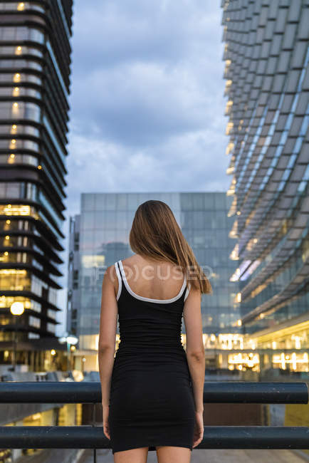 Visão traseira da jovem mulher vestindo vestido preto na cidade ao entardecer — Fotografia de Stock