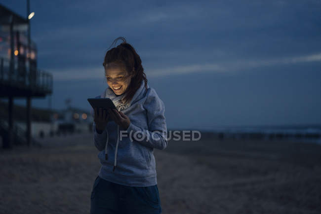 Женщина с цифровым планшетом на пляже на закате — стоковое фото