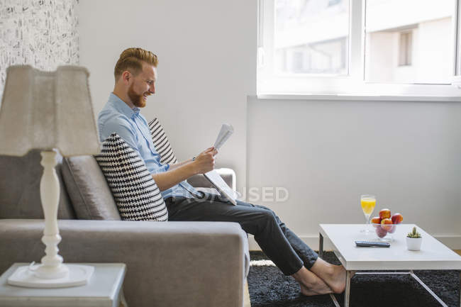Riendo hombre de negocios leyendo el periódico en su sala de estar - foto de stock