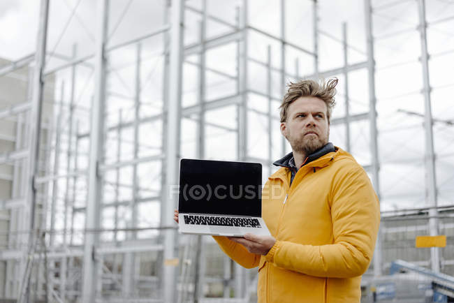 Человек держит ноутбук, строительная площадка на заднем плане — стоковое фото