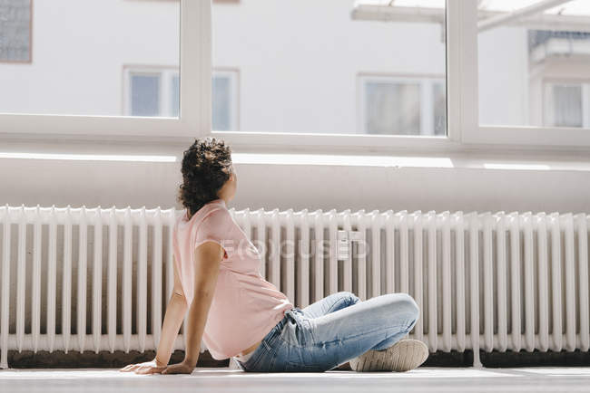 Frau sitzt auf dem Boden und schaut aus dem Fenster — Stockfoto