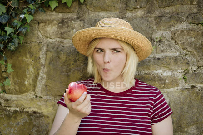 Портрет молодой блондинки в шляпе, поедающей яблоко — стоковое фото