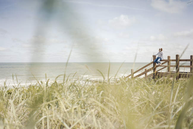 Frau sitzt auf Zaun am Meer und trägt Kopfhörer — Stockfoto