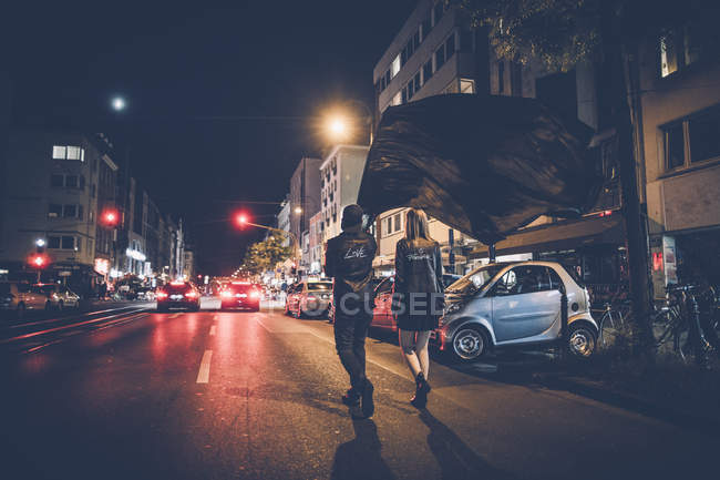 Visão traseira do jovem casal com bandeira preta andando na rua à noite — Fotografia de Stock