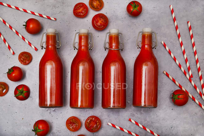 Ряд из четырех качели бутылка домашнего томатного сока, соломинки и помидоры на серой земле — стоковое фото