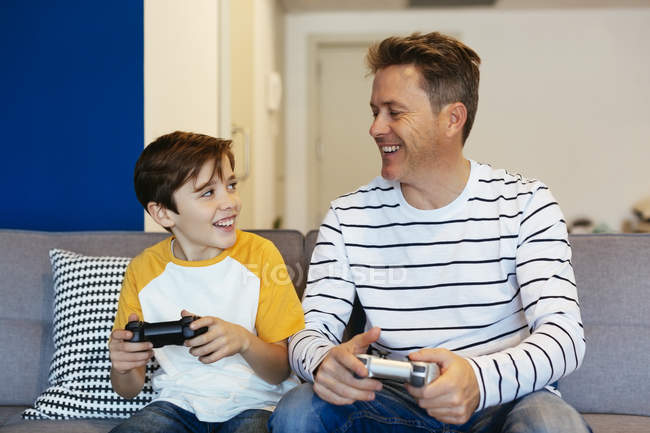 Отец и сын играют в видеоигры на диване дома — стоковое фото