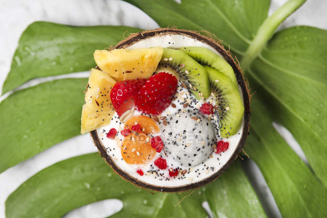 Кокосовая чаша с разнообразными фруктами, натуральным йогуртом и семенами на листе — стоковое фото