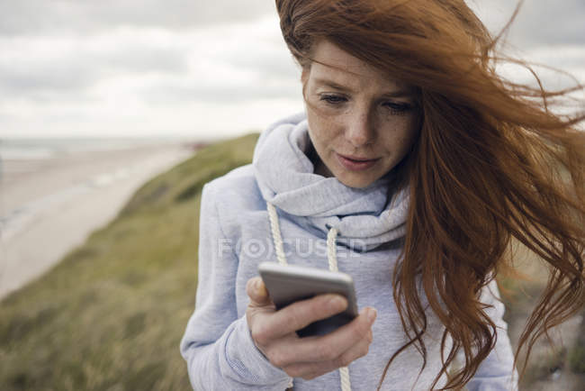 Рыжая женщина с помощью смартфона на пляже — стоковое фото