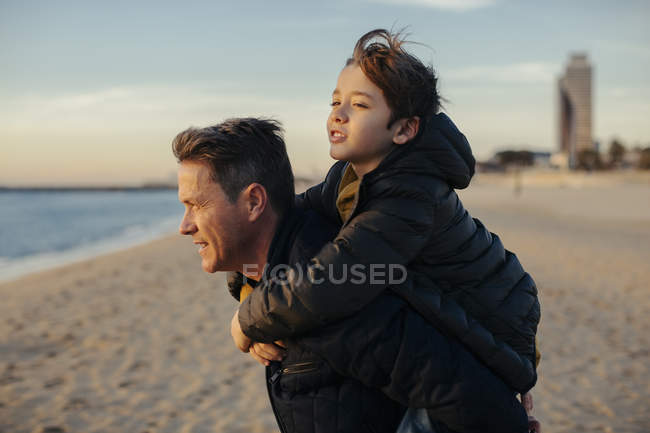 Father giving piggyback to son on beach at sunset — Stock Photo