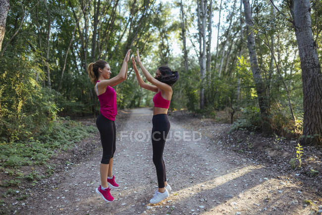 Dos mujeres activas chocando los cinco en el bosque - foto de stock