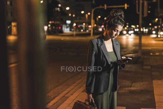 Молодий підприємець з шкіряна сумка дивлячись на стільниковий телефон вночі — стокове фото