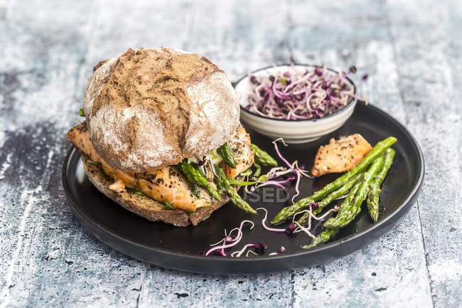 Salmon burger with green asparagus and red cress on plate — Stock Photo