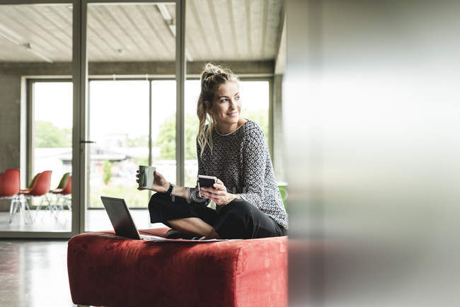 Jeune femme d'affaires travaillant dans un bureau moderne, assise sur un tabouret, utilisant un ordinateur portable — Photo de stock