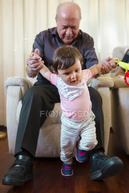 Маленька дівчинка вчиться ходити з допомогою свого дідуся вдома. — стокове фото