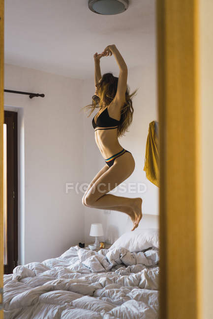 Giovane donna in biancheria intima saltando sul letto — Foto stock