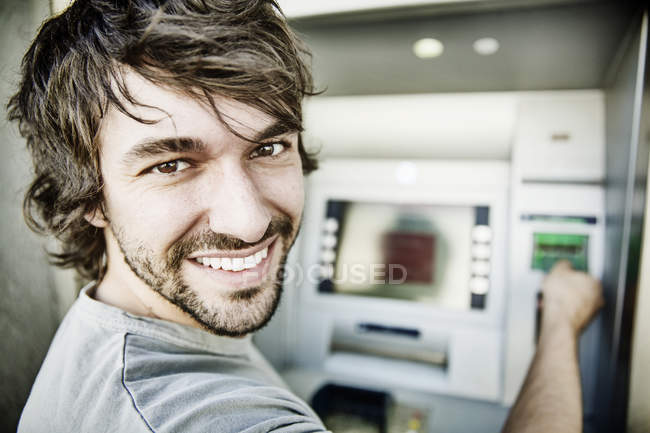 Retrato do jovem rindo usando máquina de dinheiro — Fotografia de Stock