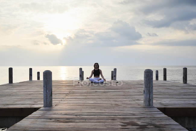 Junge Frau praktiziert Yoga auf einem Steg am Meer bei Sonnenuntergang, meditiert — Stockfoto