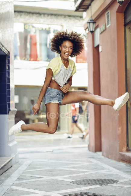 Щаслива жінка з афро зачіскою стрибає на смузі — стокове фото