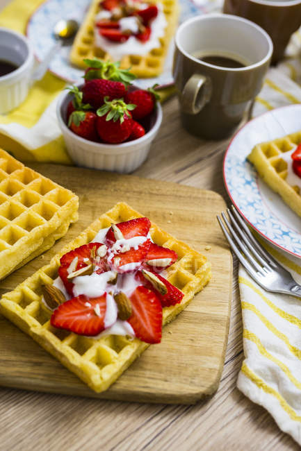 Waffle garnished with strawberries, Greek yogurt and almonds on breakfast table — Stock Photo
