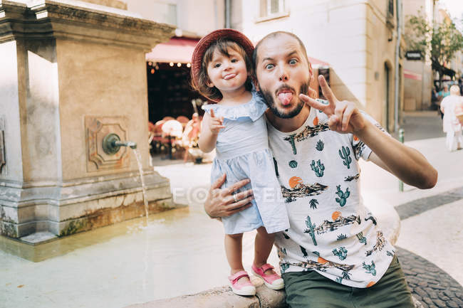 France, Aix-en-Provence, funny toddler girl and father with tongue out next to a fountain in the city — Stock Photo