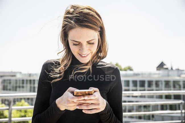 Messaggi di testo donna sorridente sulla terrazza sul tetto — Foto stock
