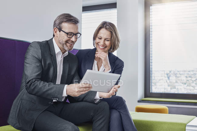 Hombre de negocios sonriente y mujer de negocios usando tableta en el salón de oficina juntos - foto de stock