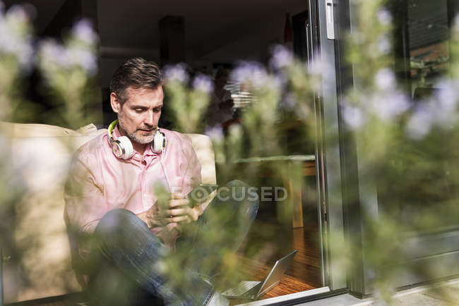 Homme mûr assis à la porte ouverte de la terrasse en utilisant smartphone — Photo de stock
