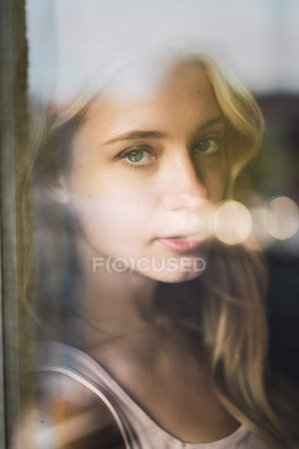 Retrato de mujer joven detrás del cristal de la ventana - foto de stock