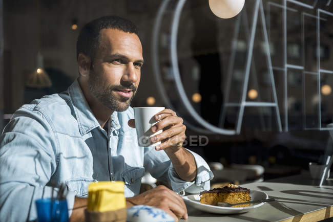 Hombre sonriente bebiendo café y comiendo pastel en un café — una persona,  luz solar - Stock Photo | #268289634