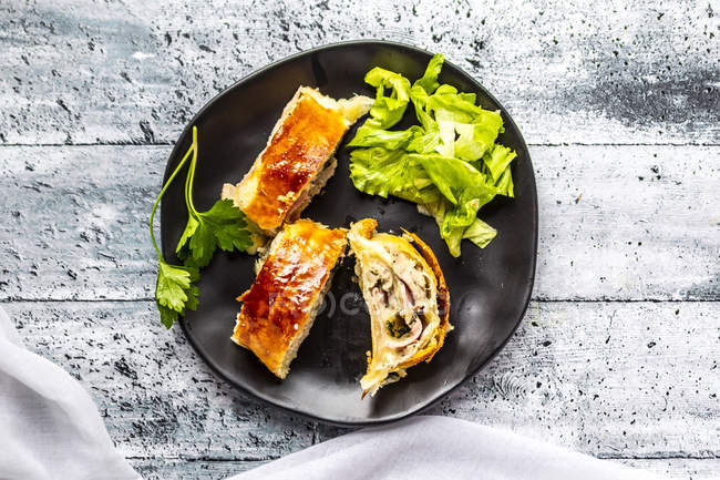 Swiss roll, puff pastry with sausage meat, cheese, onion, parsley and salad on plate — Stock Photo