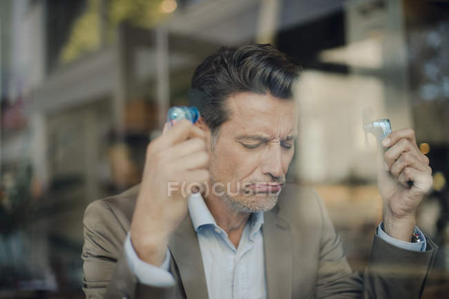 Mature businessman sitting in coffee shop, holding mini fans — Stock Photo