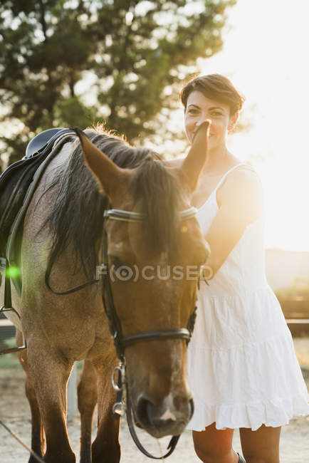 Portrait of smiling woman standing besides riding horse at backlight — Stock Photo