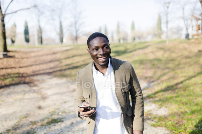 Портрет молодого человека в парке, в куртке, с смартфоном в руках — стоковое фото