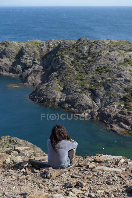Hombre mirando sentado en las rocas, mirando al mar - foto de stock