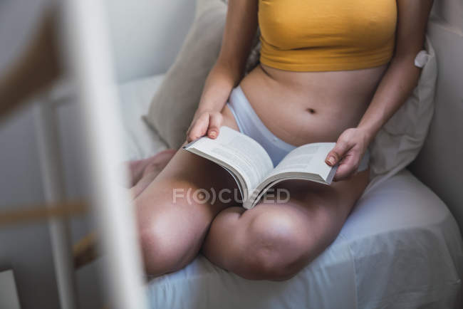 Primer plano de la mujer en el libro de lectura de ropa interior en casa - foto de stock