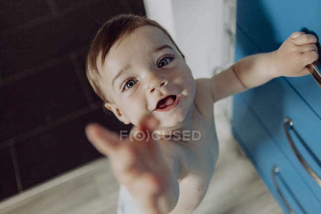 Laughing baby boy holding on to chest of drawers, reaching up — Stock Photo