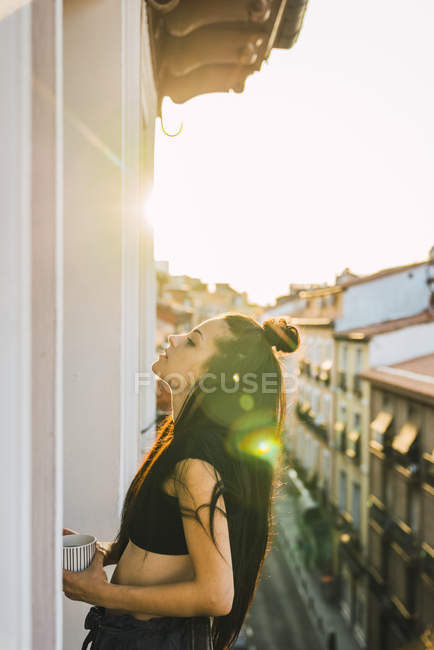 Attraente giovane donna in piedi sul balcone sopra la città al tramonto — Foto stock