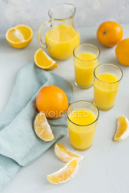 Vasos de zumo de naranja recién exprimido y naranjas - foto de stock